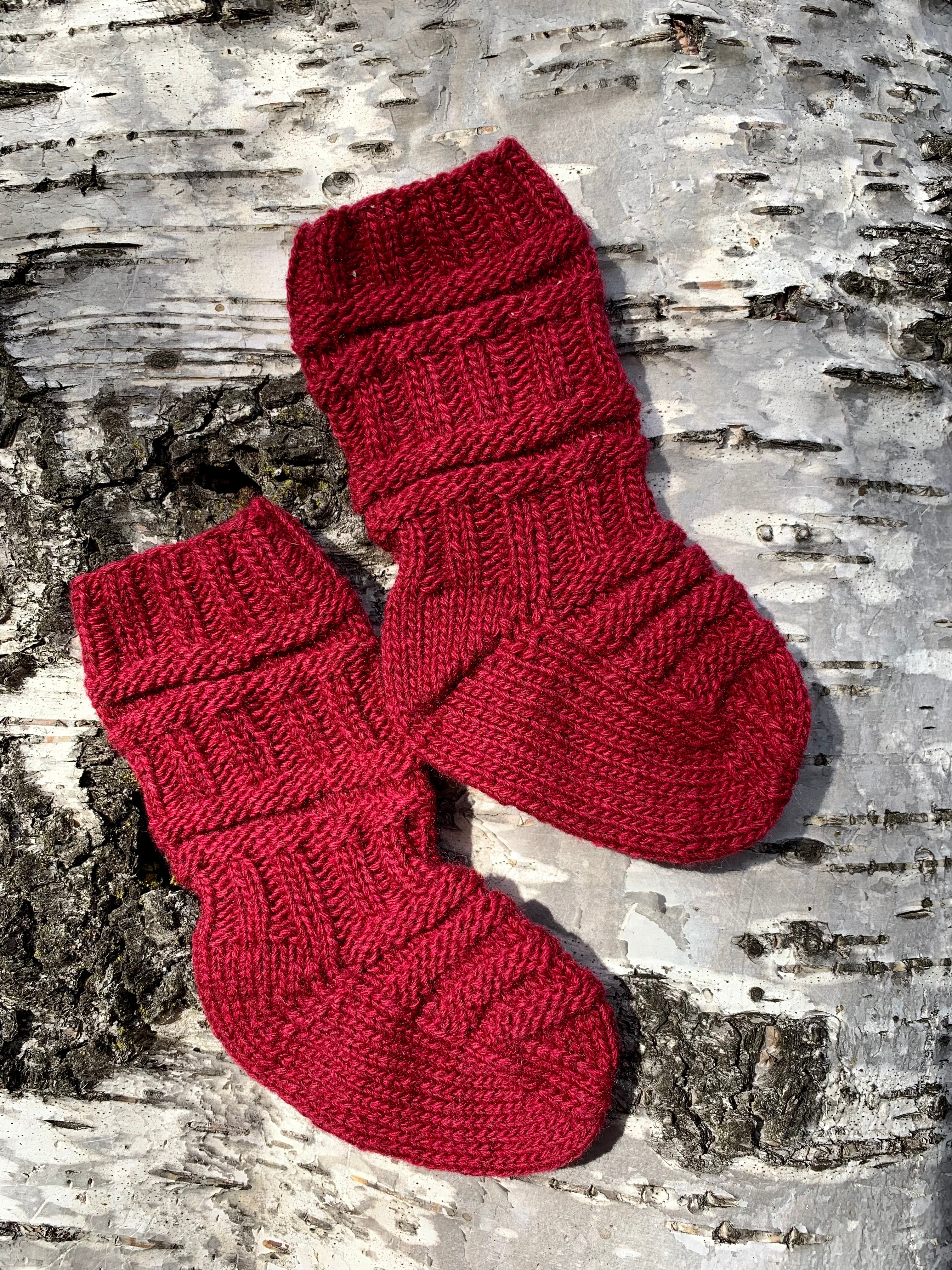 Ein Paar gestrickte Zugsocken aus rotem Kaschmir auf Birkenrinde