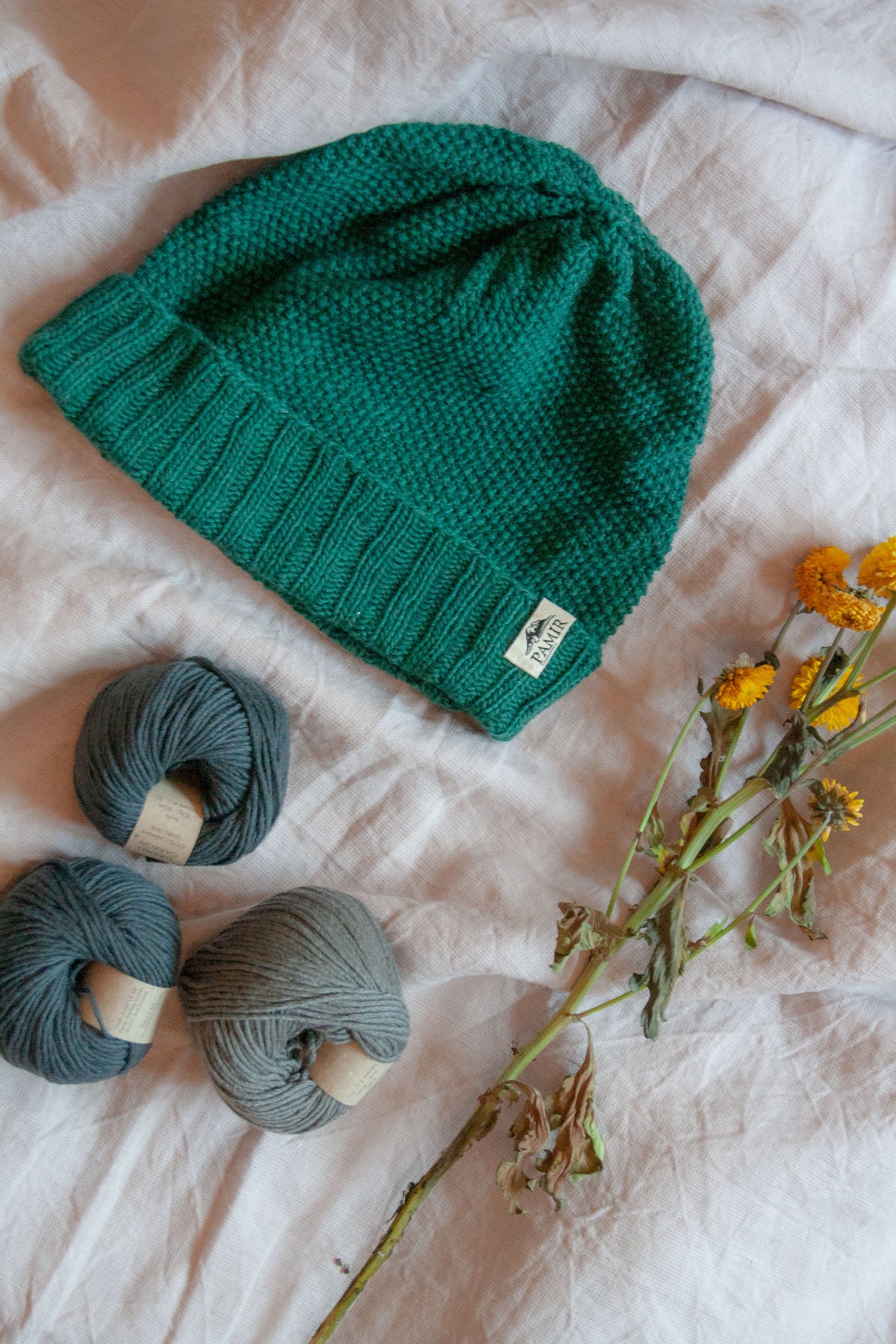 Grüne Beanie N#2 neben Kaschmirknäueln und Blumen