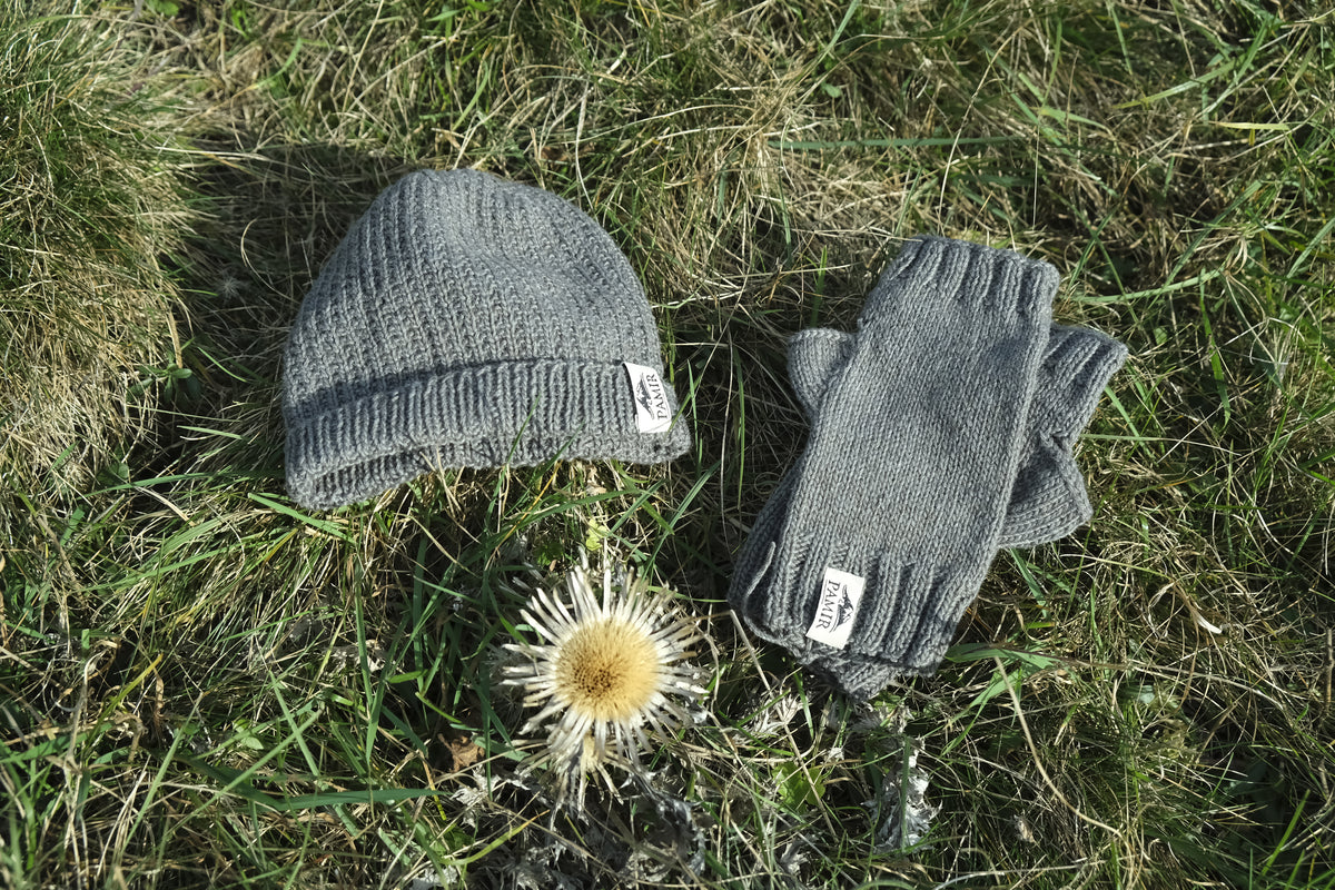 Graue Kaschmirmütze und Halbhandschuhe aus Pamir Kaschmirgarn auf einer Wiese