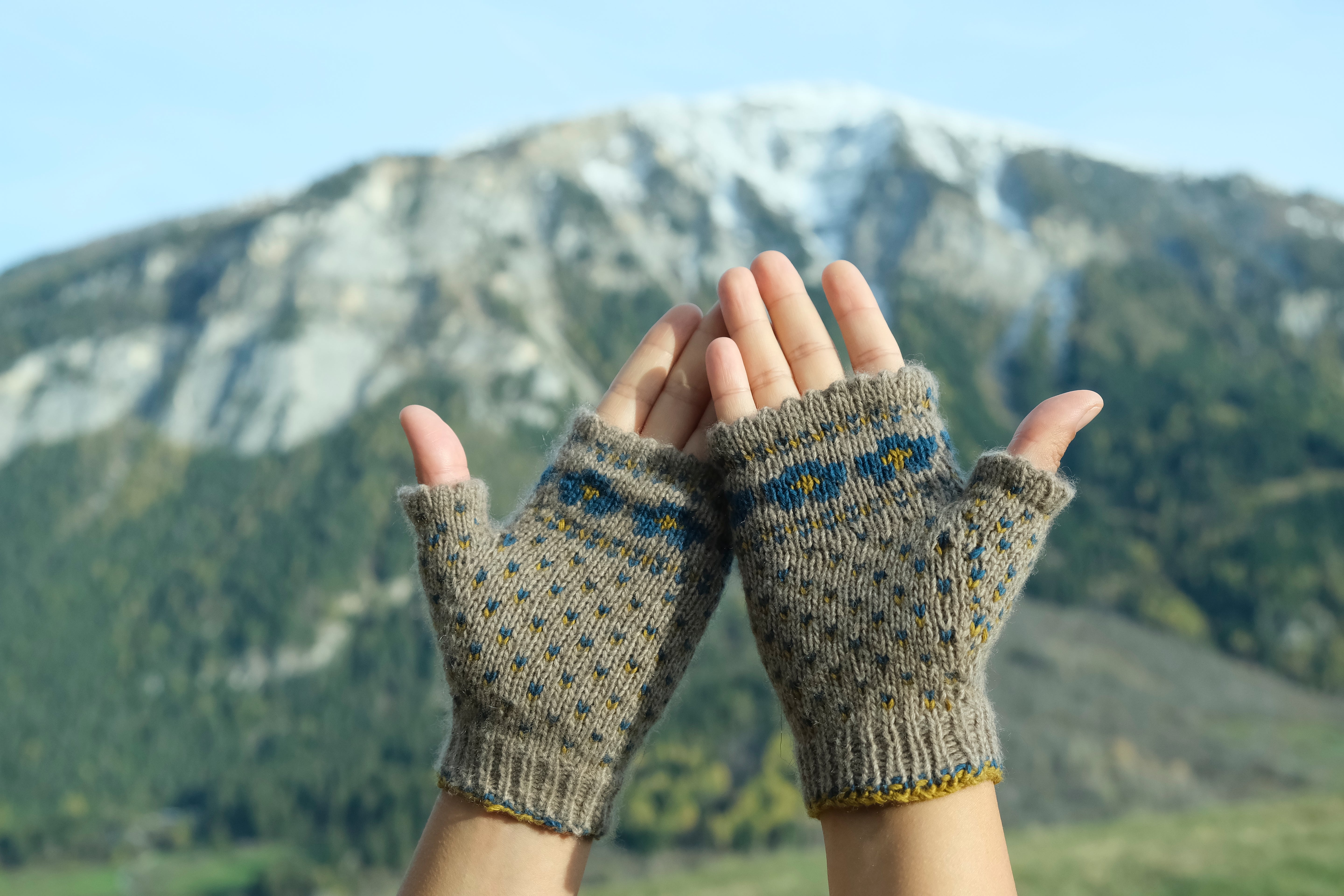 Fingerlose Handschuhe aus Kaschmir vor einer Berglandschaft