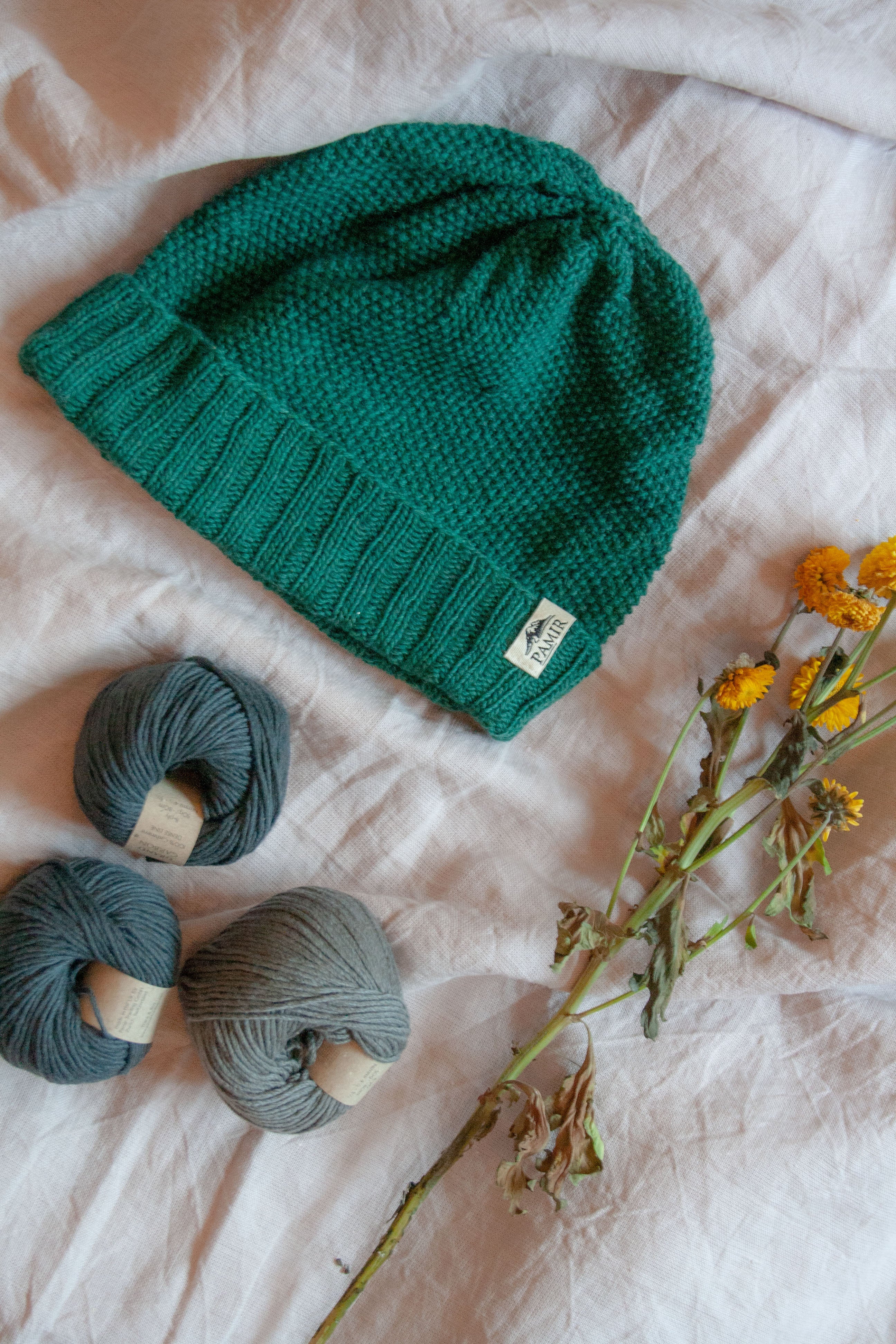 Grüne Beanie N#2 neben Kaschmirknäueln und Blumen