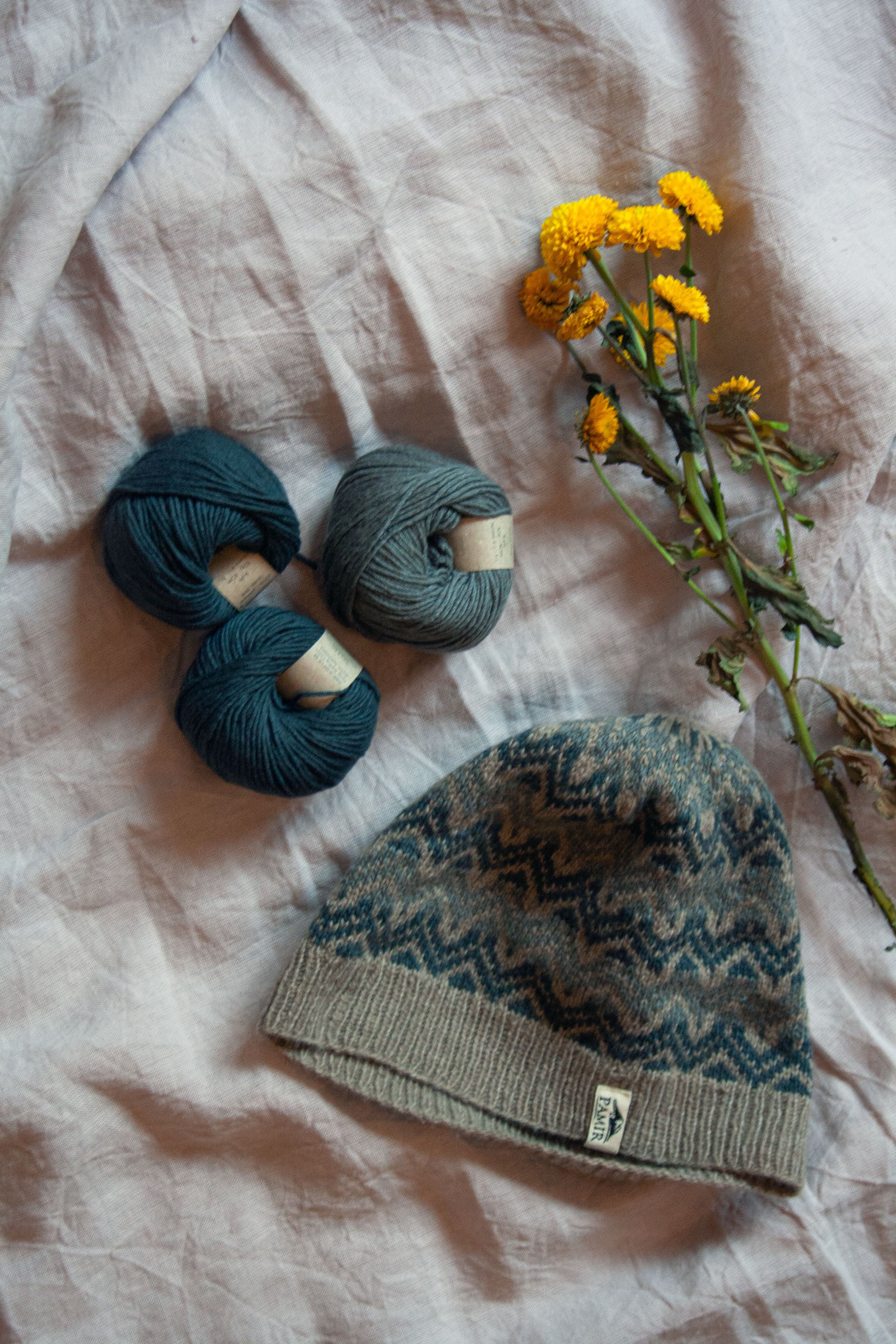 Fair-Isle-Beanie We love Wool aus SUPERIOR Kaschmirgarn neben Knäueln und Blumen