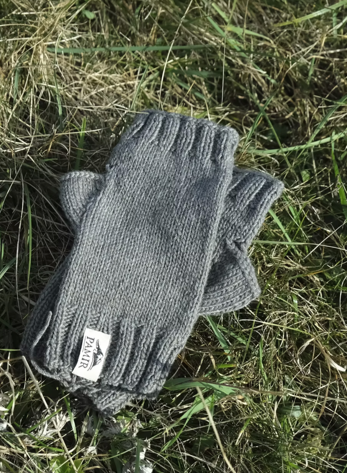 Graue Halbhandschuhe aus Pamir Kaschmir mit Etikett auf einer Wiese