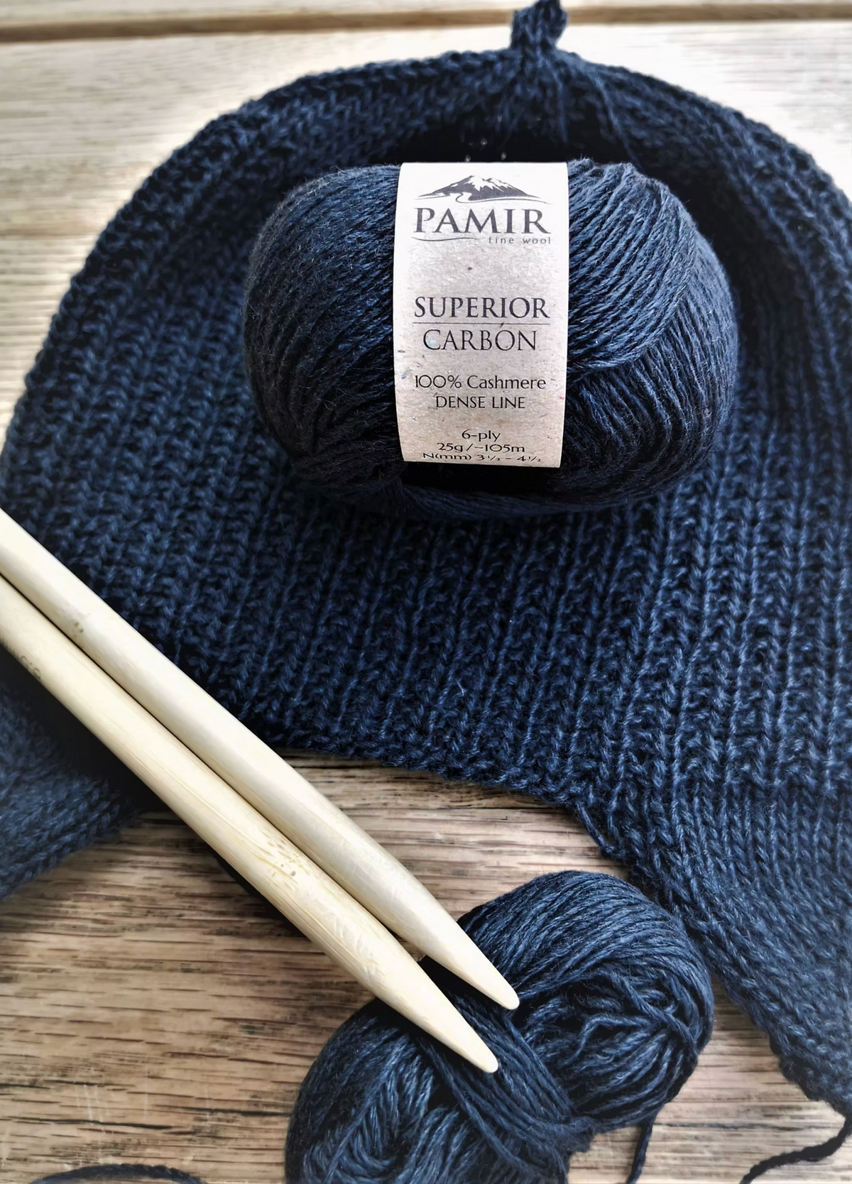 Kindermütze N#1 in Carbon neben Stricknadeln und einem Knäuel Kaschmirgarn